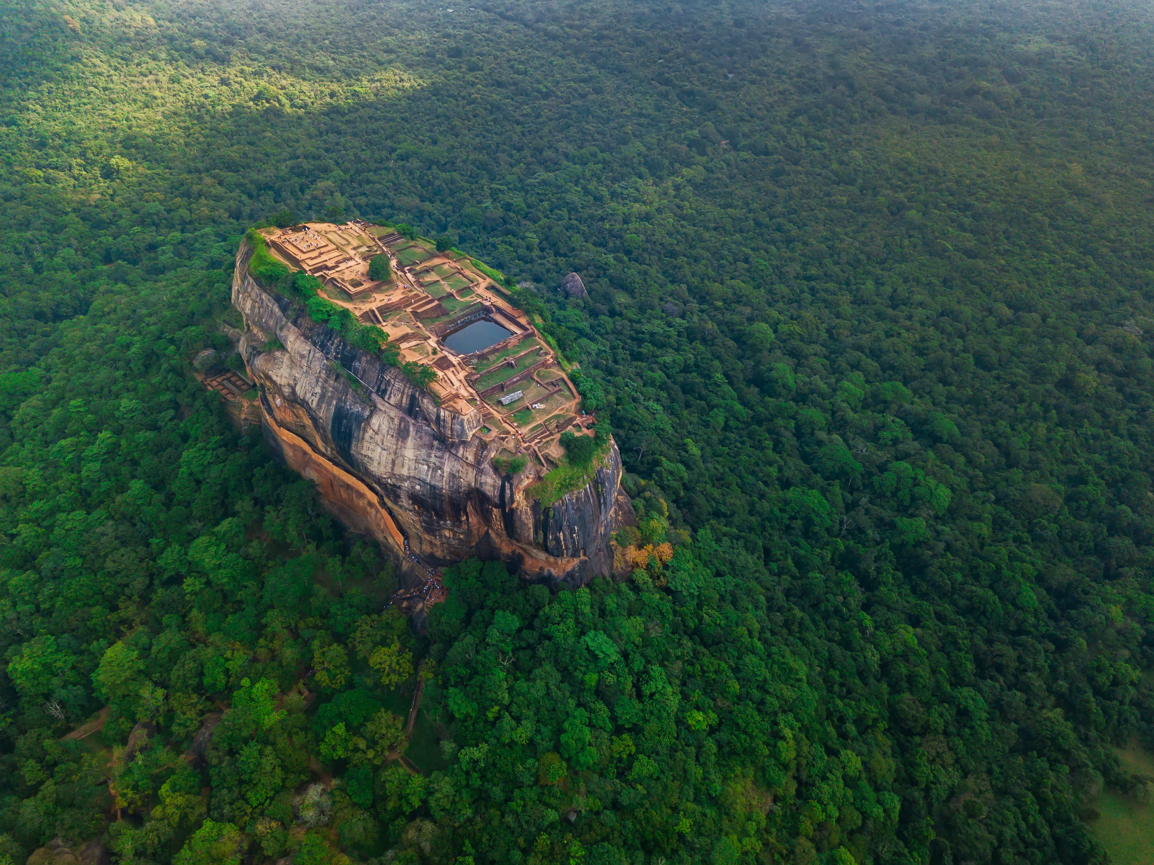 Aerial drone view of Sigiriya ancient rock fortress rising above misty emerald jungle at dawn, Sri Lanka